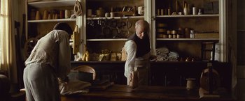 Movie still from “12 Years a Slave” (2013), directed by Steve McQueen – An old man standing in front of a wooden table; Medium shot, Over the shoulder angle