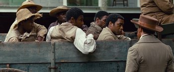 Movie still from “12 Years a Slave” (2013), directed by Steve McQueen – A group of men sitting on top of a wooden box; Medium shot, Over the shoulder angle
