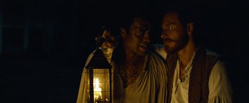 Movie still from “12 Years a Slave” (2013), directed by Steve McQueen – A man holding a lantern while another man stands next to him; Medium shot, Over the shoulder angle