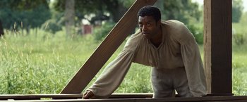 Movie still from “12 Years a Slave” (2013), directed by Steve McQueen – A black man in a brown shirt holding a wooden plank; Medium shot, Over the shoulder angle