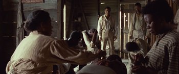 Movie still from “12 Years a Slave” (2013), directed by Steve McQueen – A man standing next to another man in front of a building; Wide shot, Over the shoulder angle