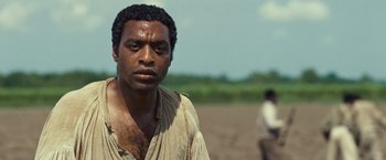 Movie still from “12 Years a Slave” (2013), directed by Steve McQueen – A black man in a white shirt is standing in a field; Close Up shot, Over the shoulder angle