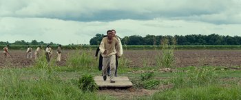 Movie still from “12 Years a Slave” (2013), directed by Steve McQueen – Two men walking across a wooden bridge in a field; Wide shot, Over the shoulder angle