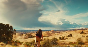 Movie still from “127 Hours” (2010), directed by Danny Boyle – A person riding a bike on a dirt road; Extreme Wide shot, Low angle