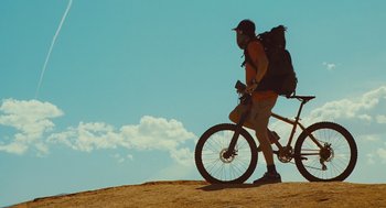 Movie still from “127 Hours” (2010), directed by Danny Boyle – A man with a backpack is standing next to a bicycle; Wide shot, Low angle