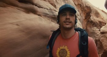 Movie still from “127 Hours” (2010), directed by Danny Boyle – A man with a backpack and a hat is standing in front of a rock wall; Close Up shot, Low angle