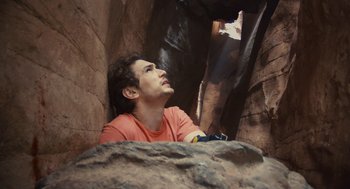Movie still from “127 Hours” (2010), directed by Danny Boyle – A man in a red shirt is looking up at the sky; Medium shot, Low angle