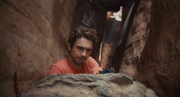 Movie still from “127 Hours” (2010), directed by Danny Boyle – A man in an orange t - shirt is in a cave; Medium shot, Low angle