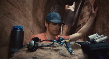 Movie still from “127 Hours” (2010), directed by Danny Boyle – A man in a baseball cap is holding a pair of headphones; Medium shot, Overhead angle
