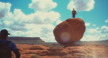 Movie still from “127 Hours” (2010), directed by Danny Boyle – A man standing on top of a large rock in the middle of the desert; Extreme Wide shot, Low angle