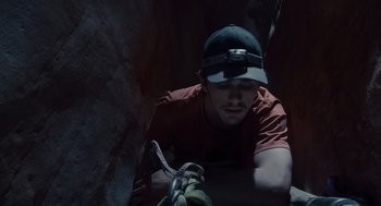 Movie still from “127 Hours” (2010), directed by Danny Boyle – A man in a red shirt and a hat climbing a rock wall; Close Up shot, Low angle
