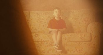 Movie still from “127 Hours” (2010), directed by Danny Boyle – A young boy sitting on a couch in a living room; Medium shot, High angle