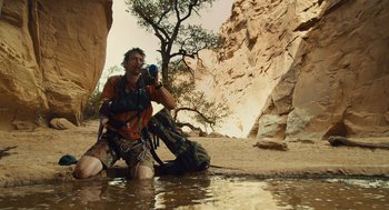 Movie still from “127 Hours” (2010), directed by Danny Boyle – A man kneeling down in the water taking a picture; Wide shot, Low angle