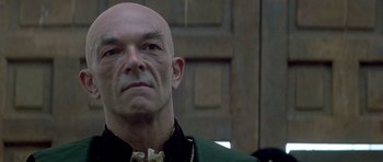 A bald man in a green jacket looking at the camera