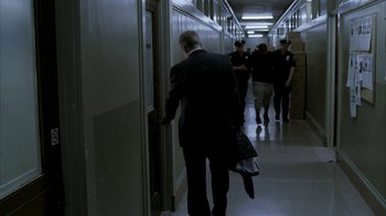 Movie still from “16 Blocks” (2006), directed by Richard Donner – A man in a suit and tie walking down a hallway; Wide shot, Over the shoulder angle