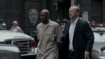 Movie still from “16 Blocks” (2006), directed by Richard Donner – Two men walking down a street in front of a police car; Medium shot, Over the shoulder angle