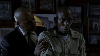 Movie still from “16 Blocks” (2006), directed by Richard Donner – Two men in a room one is holding his arm up to his shoulder; Close Up shot, Over the shoulder angle