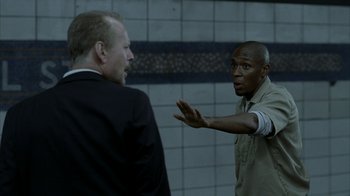Movie still from “16 Blocks” (2006), directed by Richard Donner – Two men in suits are talking in a subway station; Medium shot, Over the shoulder angle