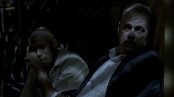 Movie still from “16 Blocks” (2006), directed by Richard Donner – A man sitting next to another man in a dark room; Close Up shot, Over the shoulder angle