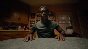 Movie still from “Snowfall” (2017), directed by Hiro Murai – A man sitting at a table in a kitchen; Medium shot, High angle
