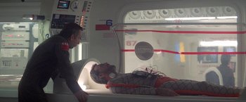 Movie still from “2010: The Year We Make Contact” (1984), directed by Peter Hyams – A man laying on a bed in a room; Medium shot, Over the shoulder angle