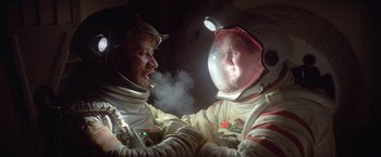 Movie still from “2010: The Year We Make Contact” (1984), directed by Peter Hyams – Two men in spacesuits are smoking in a dark room; Medium shot, Overhead angle