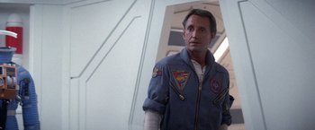 Movie still from “2010: The Year We Make Contact” (1984), directed by Peter Hyams – A man in a blue jacket standing next to a white wall; Medium shot, Low angle