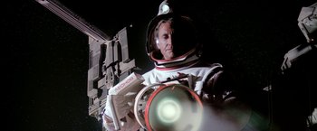 Movie still from “2010: The Year We Make Contact” (1984), directed by Peter Hyams – A man in a spacesuit is holding a device; Medium shot, Low angle