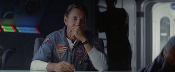 Movie still from “2010: The Year We Make Contact” (1984), directed by Peter Hyams – An older man wearing a nasa uniform sitting in front of a table; Medium shot, Over the shoulder angle