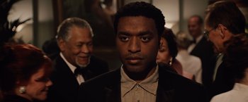 Movie still from “2012” (2009), directed by Roland Emmerich – A person wearing a suit and tie; Close Up shot, Over the shoulder angle