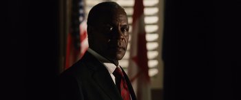 Movie still from “2012” (2009), directed by Roland Emmerich – A man in a suit and tie in front of a flag; Close Up shot, Low angle