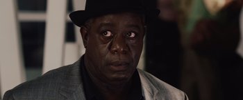 Movie still from “2012” (2009), directed by Roland Emmerich – A person wearing a suit and a hat; Close Up shot, Over the shoulder angle