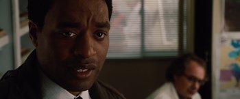 Movie still from “2012” (2009), directed by Roland Emmerich – A person wearing a suit and tie; Close Up shot, Over the shoulder angle