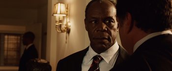 Movie still from “2012” (2009), directed by Roland Emmerich – A man in a suit and tie in front of a lamp; Close Up shot, Over the shoulder angle