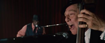 Movie still from “2012” (2009), directed by Roland Emmerich – A man singing into a microphone next to a man playing a piano; Close Up shot, Low angle