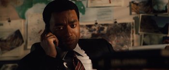 Movie still from “2012” (2009), directed by Roland Emmerich – A man wearing a suit and tie talking on a cell phone; Close Up shot, Over the shoulder angle