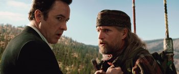 Movie still from “2012” (2009), directed by Roland Emmerich – Two men standing next to each other in front of a forest; Close Up shot, Over the shoulder angle