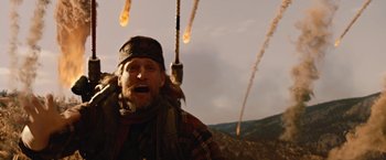 Movie still from “2012” (2009), directed by Roland Emmerich – An old man with long hair and a beard is standing in front of a bunch of smoke bombs; Medium shot, Low angle
