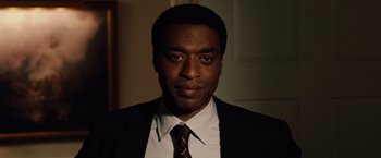 Movie still from “2012” (2009), directed by Roland Emmerich – A person wearing a suit and tie; Close Up shot, Over the shoulder angle