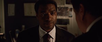 Movie still from “2012” (2009), directed by Roland Emmerich – A person wearing a suit and tie; Close Up shot, Over the shoulder angle