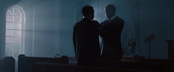 Movie still from “2012” (2009), directed by Roland Emmerich – Two men in suits are standing in the dark; Medium shot, Low angle