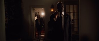 Movie still from “2012” (2009), directed by Roland Emmerich – A man in a suit and tie standing in a room with a woman; Medium shot, Low angle