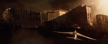 Movie still from “2012” (2009), directed by Roland Emmerich – An airplane is flying over a burning building; Extreme Wide shot, High angle