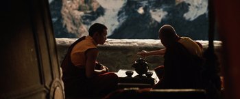 Two monks sitting on a ledge with mountains in the background