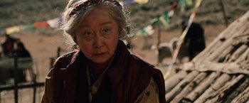Movie still from “2012” (2009), directed by Roland Emmerich – An older woman wearing a headscarf and a red jacket; Close Up shot, Low angle