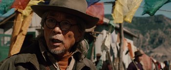 Movie still from “2012” (2009), directed by Roland Emmerich – An older man wearing glasses and a hat; Close Up shot, Over the shoulder angle