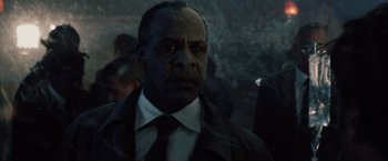 Movie still from “2012” (2009), directed by Roland Emmerich – A man in a suit and tie in a crowd of people; Close Up shot, Low angle