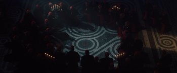 Movie still from “2012” (2009), directed by Roland Emmerich – A group of people sitting in front of candles on the floor; Extreme Wide shot, Overhead angle