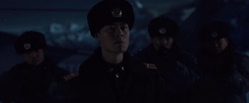 Movie still from “2012” (2009), directed by Roland Emmerich – A man in a military uniform is looking at the camera while another man is standing behind him; Close Up shot, Low angle