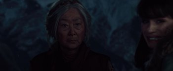 Movie still from “2012” (2009), directed by Roland Emmerich – An older woman with a gray hair and a red headband; Close Up shot, Over the shoulder angle